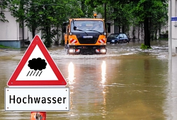 Starkregen Ein Unimog fährt durch eine vom Wasser überflutete Straße. Vorne ein Schild "Hochwasser".